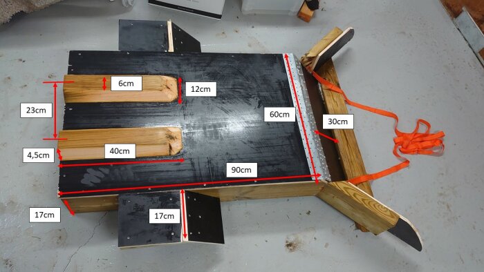 Hemmagjord träsled med måttmarkeringar och bärrem på ett betonggolv.