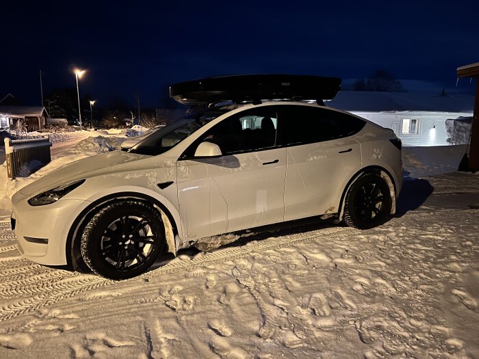 Vit Tesla Model Y med takbox parkerad i snöigt landskap på natten.