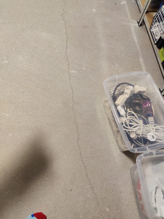 Golv med spricka, genomskinliga plastlådor med sladdar, del av butiksinteriör.