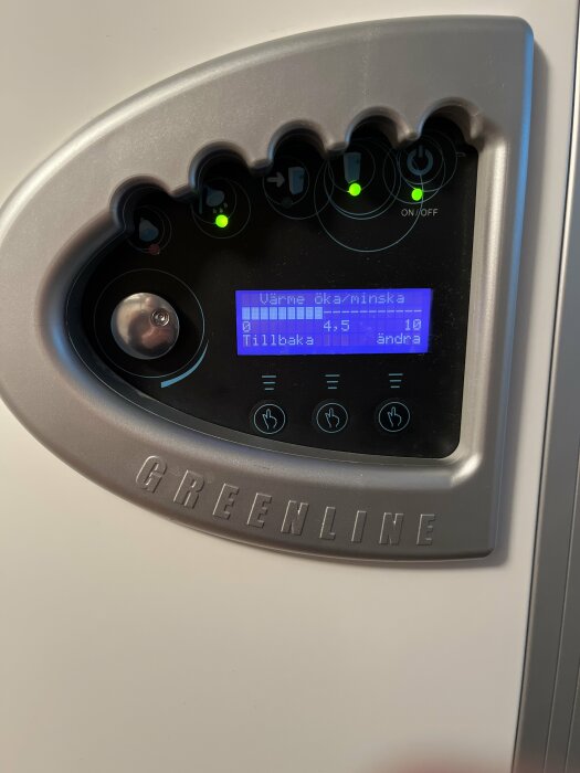 Kontrollpanel med knappar och display, texten "Värme öka/minska", "GREENLINE", och symboler för justering och ström.