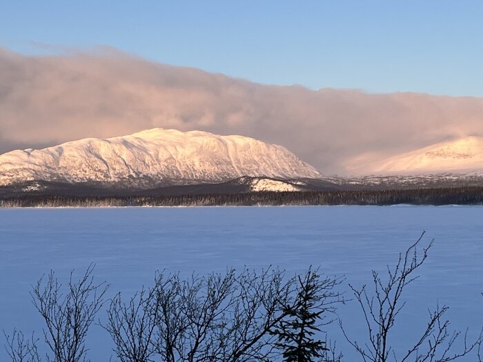 Snötäckt bergslandskap, isbelagt vatten, molnstrimma, vinterskog, soluppgång eller solnedgång, stilla, naturlig skönhet.