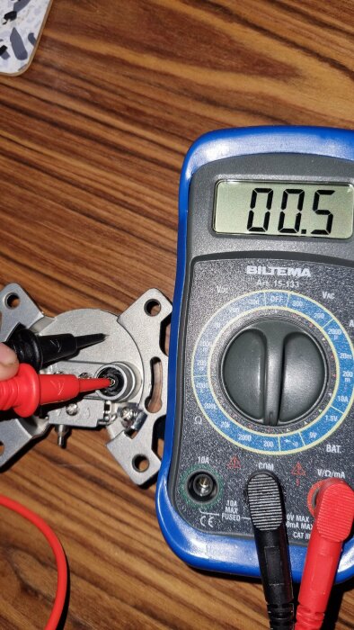 Multimeter mäter elektrisk komponent, visar 0.5 Ohm, mätspetsar anslutna, träbakgrund, tekniskt arbete.