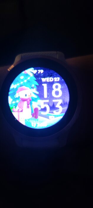 Smartklocka visar färgglad juldisplay med tecknad pingvin, tid, dag och datum.