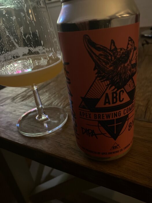 Ölglas med skum vid kanten och en färgglad burk från Apex Brewing Company med en bild av en varg.