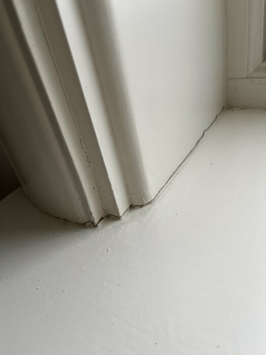 Vit, sprucken fönsterbräda nära radiator, behov av underhåll eller reparation.