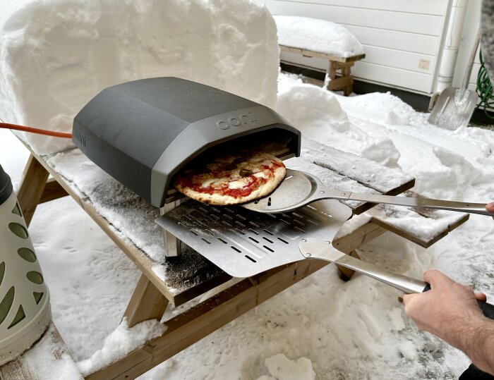 Portabel pizzaugn utomhus på vintern, person tar ut pizza, snöigt.