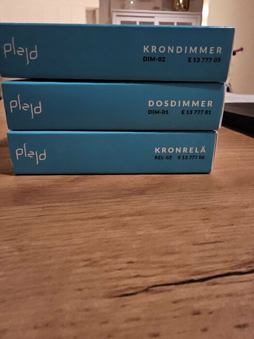 Tre blåa förpackningar från Plejd, märkta "KRONDIMMER," "DOSDIMMER," och "KRONRELÄ" på ett träbord.