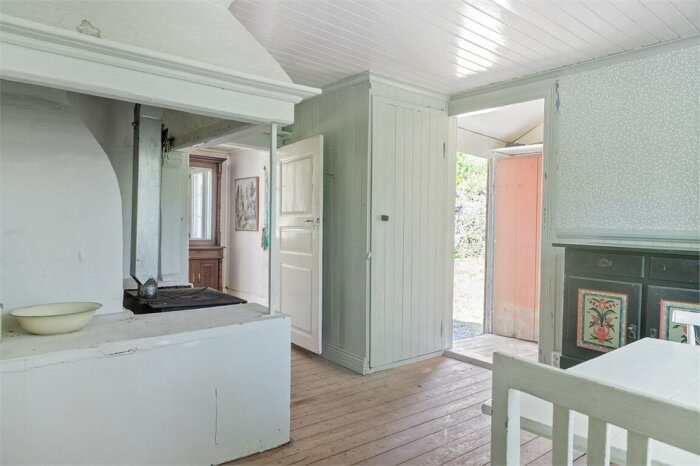 Gammaldags kök med spis, vit träpanel, öppen dörr och ljusinsläpp. Vintage interiörstil.