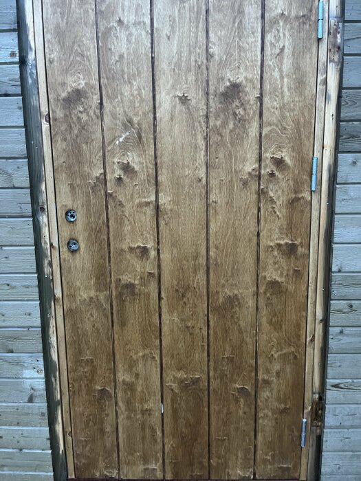 En brun trädörr, vertikala paneler, lås, gångjärn, utanpåliggande trädetaljer, sliten, traditionell.