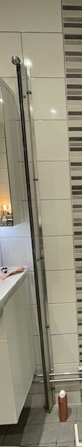 Modernt badrum, duschhörna med glasdörrar, kakelväggar, radiator, handduk, delvis synlig handfat.