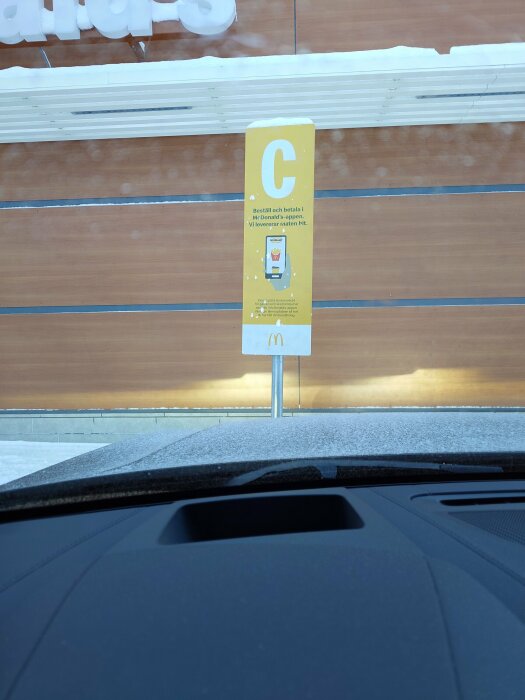 Skylt vid McDonald's drive-thru med instruktioner, sett från bilens förarsida.