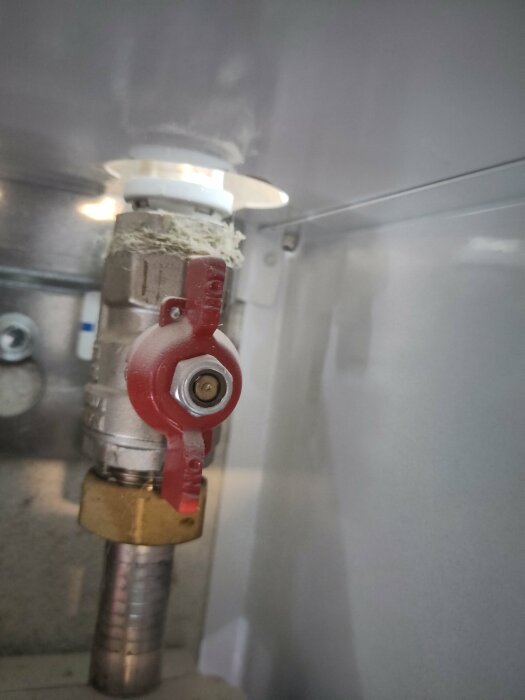 Rörkoppling med röd ventil och isbildning mot grå bakgrund. Frost eller kylsystemläckage synligt.
