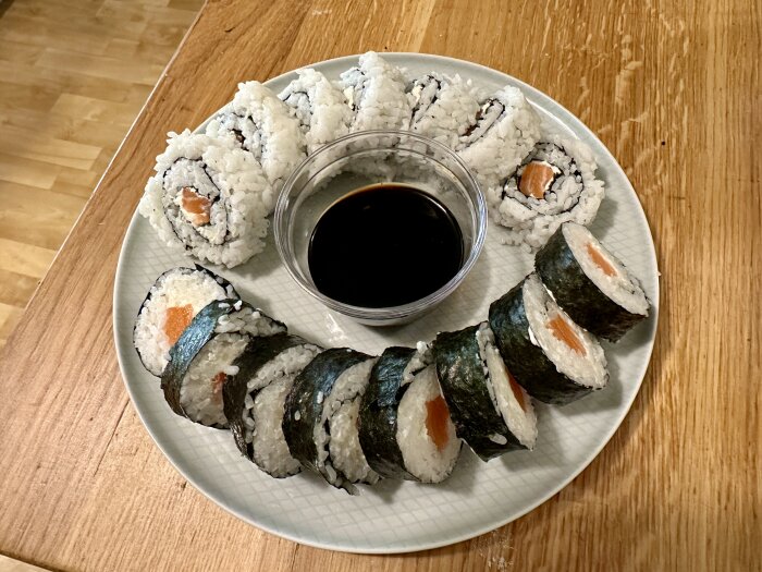 En tallrik med sushi, inklusive maki och nigiri, serveras med sojasås på ett träbord.