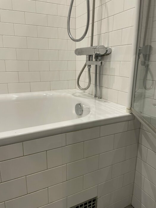 Modernt badrum med vitt kakel, badkar, duschset, och glasduschvägg.