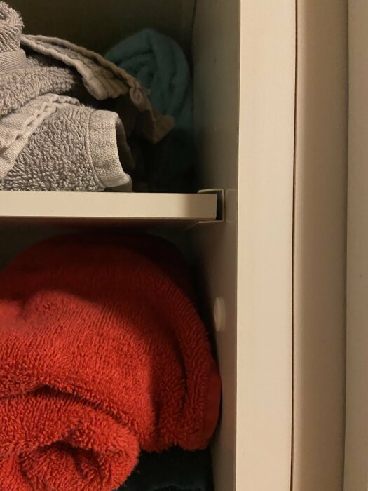 Ett öppet skåp med två fack, övre fylld med gråa handdukar, och den nedre med stor röd handduk.