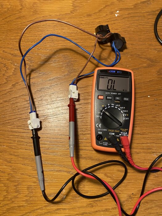 Multimeter och kablar på träbord, potentiell elektrisk krets eller testuppställning.