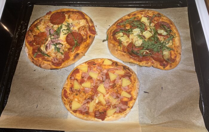 Fyra hembakade pizzor på bakplåtspapper: varierade toppings som pepperoni, skinka, ananas, artichoke och ruccola.