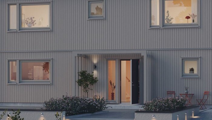 Tvåvåningshus i skymning, tända ljus, öppen dörr, skandinavisk stil, planteringar utanför, lugnt bostadsområde.