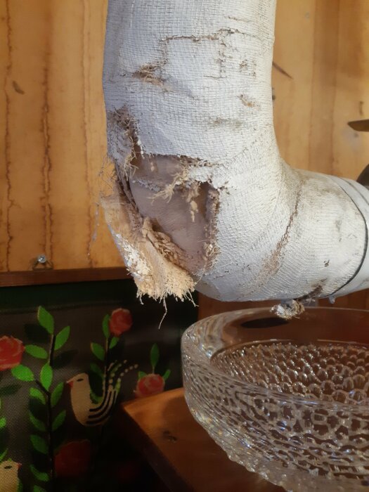 Slitet tygfodral på rör, träyta, genomskinlig glasskål, målad tavla med blommor och fågel.