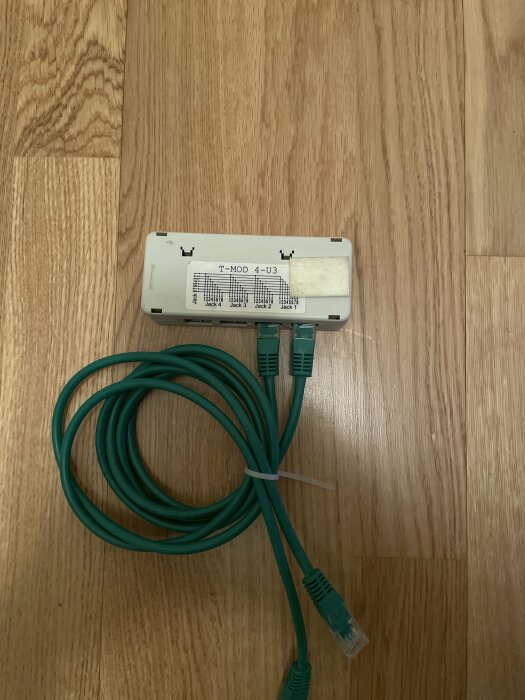 Telefonadapter och grönt nätverkskabel på trägolv.