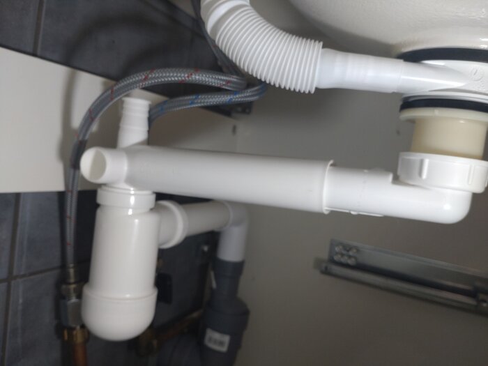 VVS-installation under diskbänk med rörledningar, avlopp och flexibla slangar.