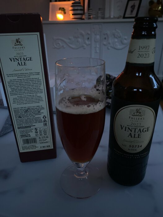 Ett glas öl, Fuller's Vintage Ale-flaska och kartong. Hemtrevlig bakgrund, skymning. Limited Edition, alkoholhalt noterad.