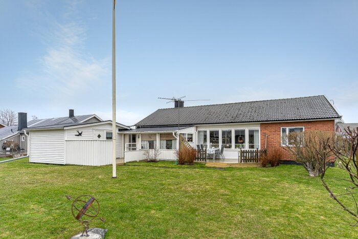 Enfamiljshus med tegelfasad, veranda, gräsplan, flaggstång och molnig himmel.