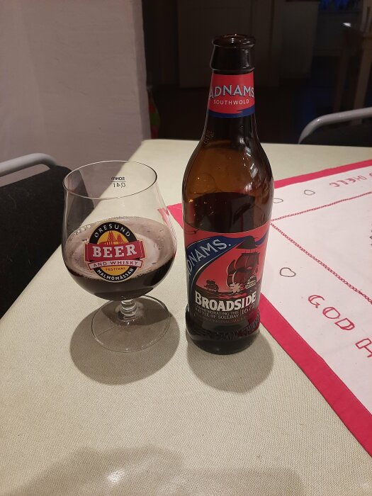 Ölflaska och fyllt glas på bord, Adnams Broadside, ölprovarglas, bakgrund av köksinredning.