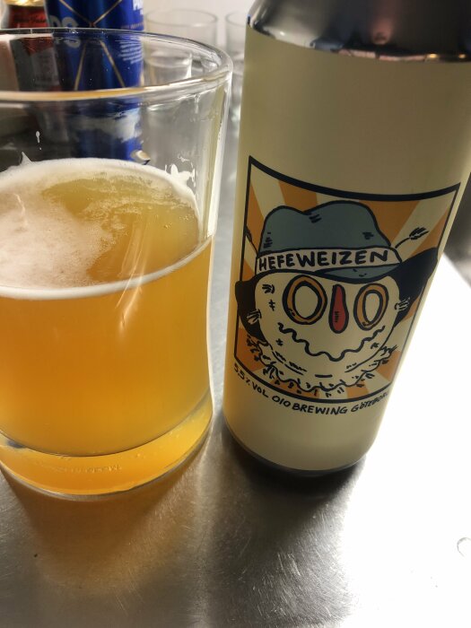 Ett glas ljus öl och en ölflaska med etikett "Hefeweizen 010 Brewing" på en metallyta.