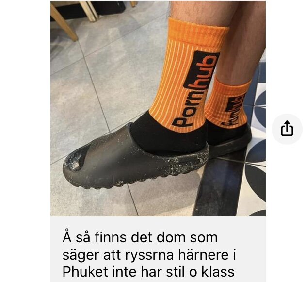 Person bär orange strumpor med PornHub-logotyp, svarta skor, text hävdar ryssars stilbrist i Phuket.