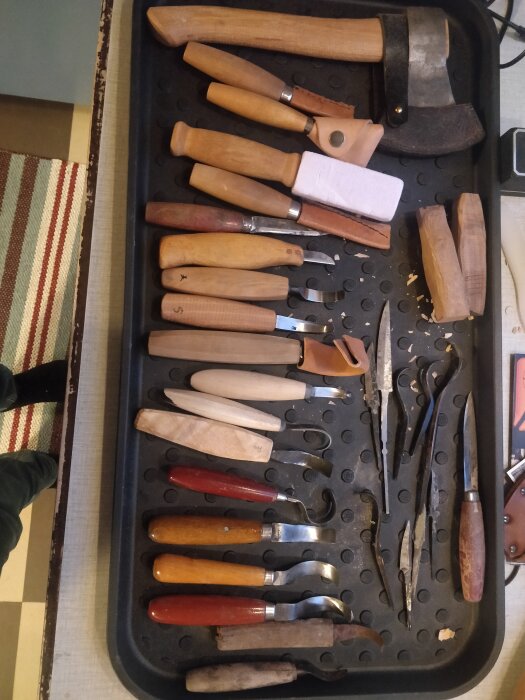 Ett sortiment av träsnideriverktyg och en yxa på ett ordnat verktygsfack.