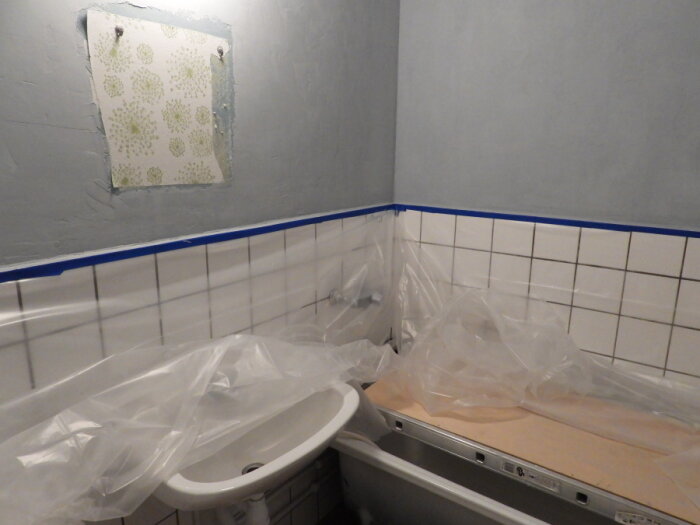 Badrum under renovering, toalett täckt med plast, kakel, ej färdigmålad vägg, osammanhängande inredning.