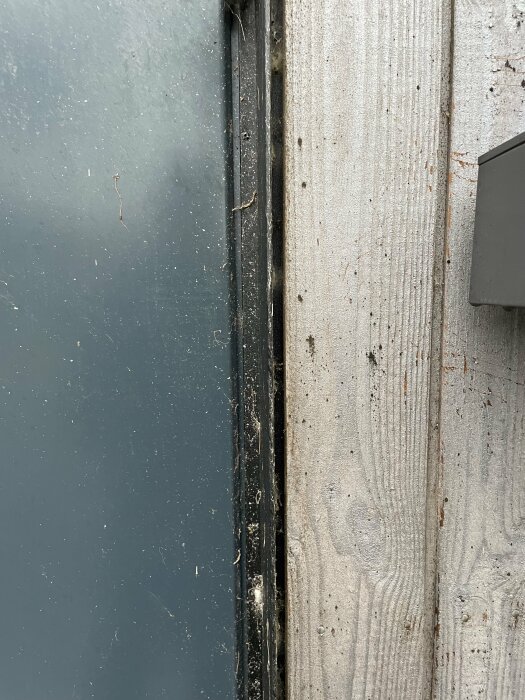 Slitet dörrparti, smutsigt, trä och metall, svart, grå. Möjliga tecken på försummelse eller åldring.