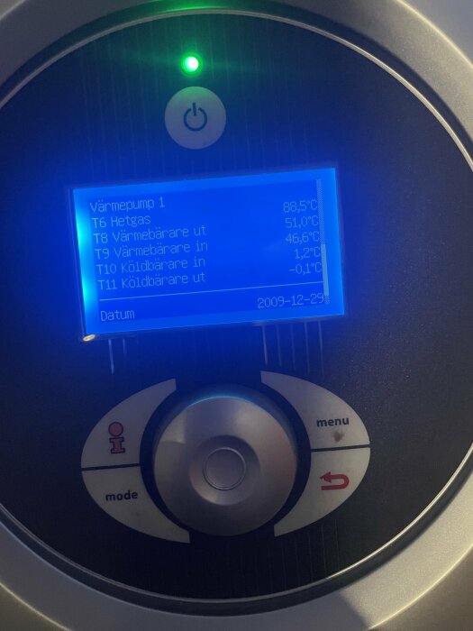 Digital display på värmepump visar temperaturer och status med knappar för inställningar och information. Datum visar 2009-12-29.