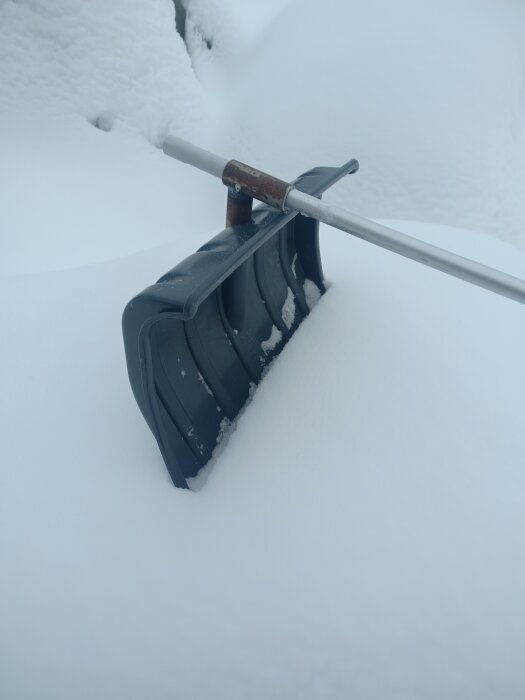 Snöskyffel delvis begravd i tjockt lager av vit snö.