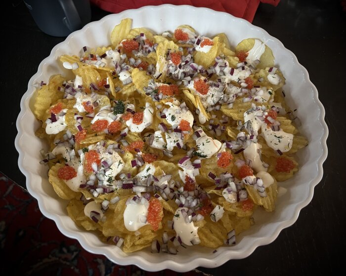 Potatischips med lök, gräddfil, kryddor och röd kaviar i serveringsskål.