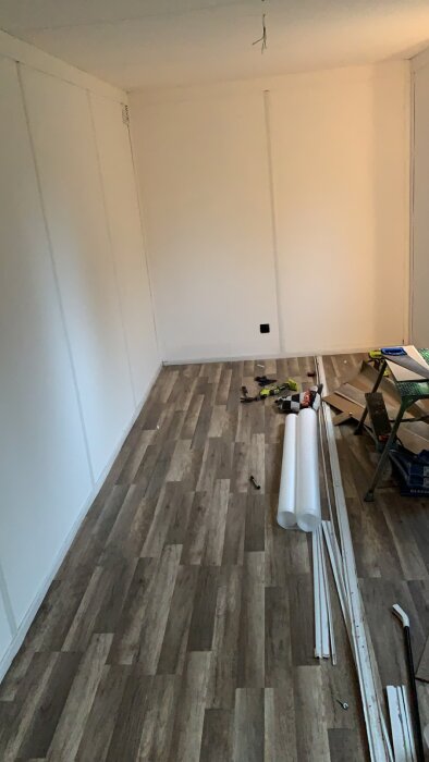 Ett tomt rum under renovering med nytt laminatgolv, verktyg och byggmaterial på golvet.