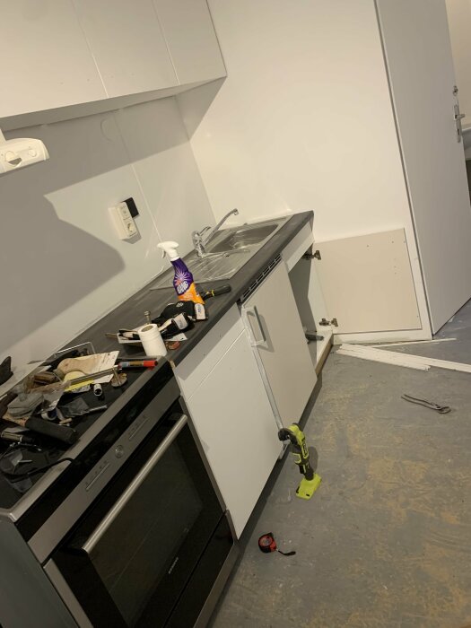 Stökigt kök under renovering eller reparation med öppen diskmaskin och verktyg utspridda.