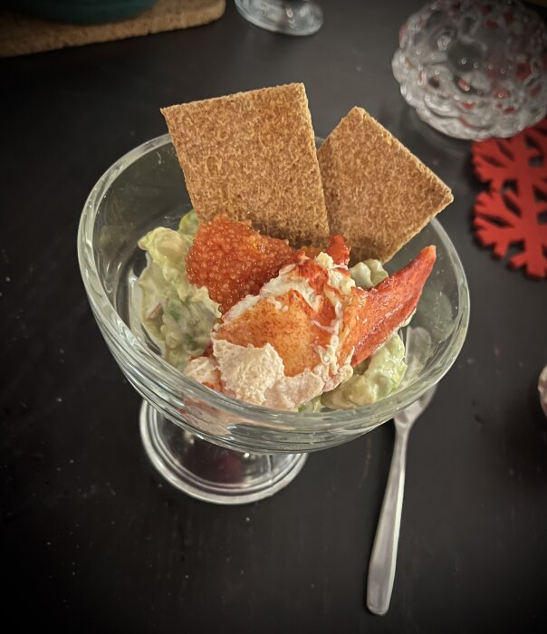 Räksallad med kaviar och knäckebröd i en glasskål på ett mörkt bord.