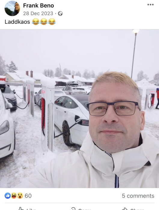 Man i snöig parkering framför laddstationer med bilar, delar en selfie med humörfyllda emojis.