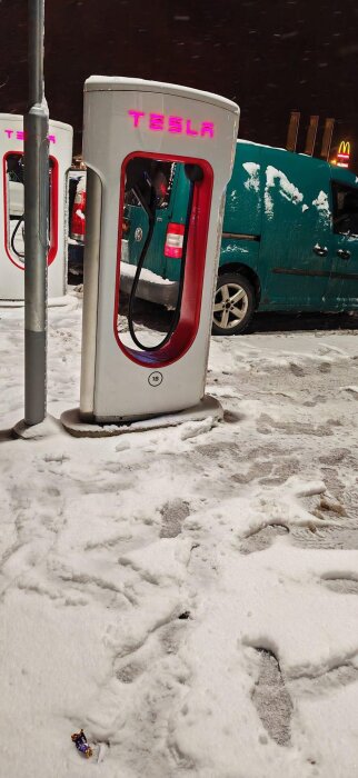 Tesla Supercharger-station, snötäckt, natt, McDonald's-skylt i bakgrunden, fotspår i snön.