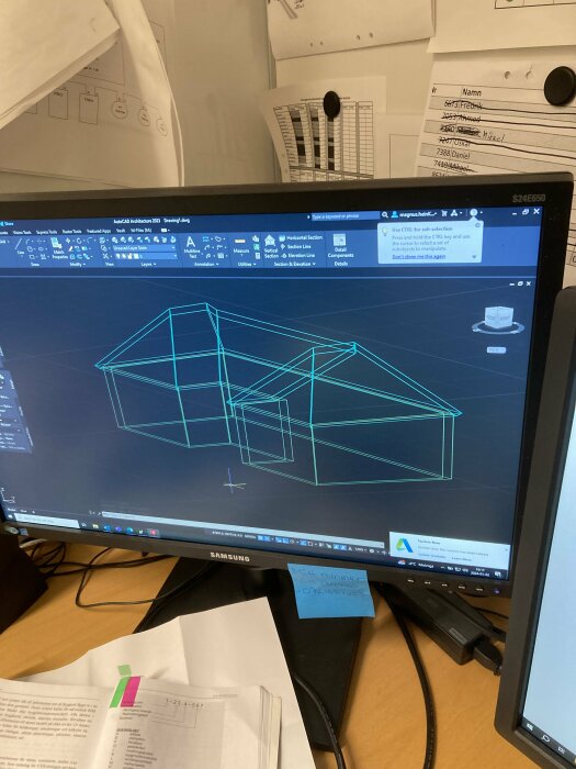 Skärm med CAD program, ritning av hus, kontorsmiljö, papper, post-it-lappar.