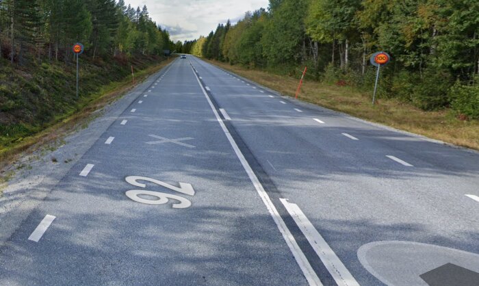 Tom landsväg genom skog med hastighetsgränsskyltar som visar 100 km/h, avfartsmarkering, inga fordon synliga.