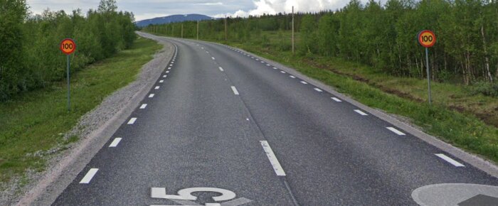 Asfalterad landsväg, dubbla körbanor, fartgränsskyltar, skogsbeklädda sidor, disigt väder, ingen synlig trafik.