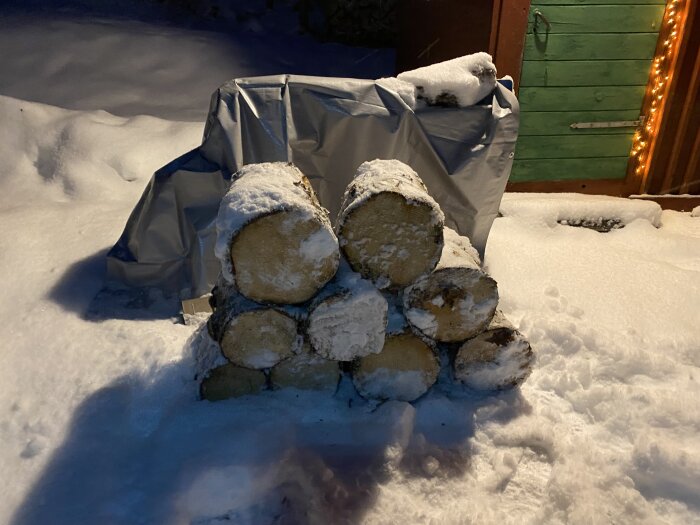 Vedtrave täckt av snö på kvällen, med grannt ljus och snötäckt mark.