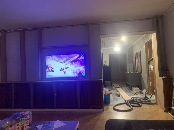 Vardagsrum under renovering med TV-spel på skärmen, leksaker på golvet och oavslutad golvbeläggning.