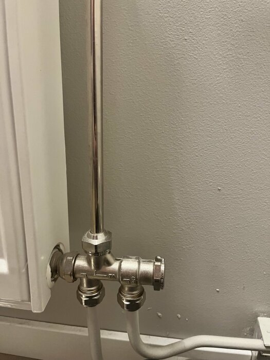 Metall rörkoppling och ventiler vid vägg, ansluten till värmerör, industriell estetik, inomhus bostadsinfrastruktur.