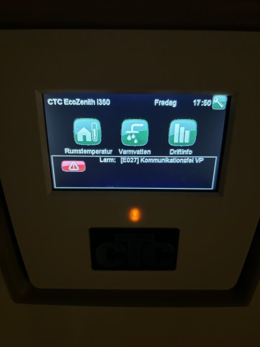 Digital display på en CTC EcoZenith i350 värmepump med felmeddelande, rumstemperatur- och varmvattenikoner, och klocka.