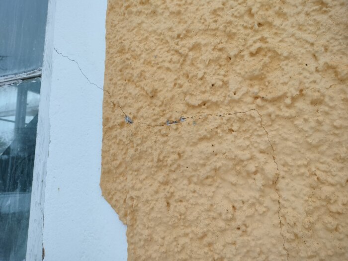Gul, sprucken fasad nära fönster, tecken på byggnadsskada eller slitage.