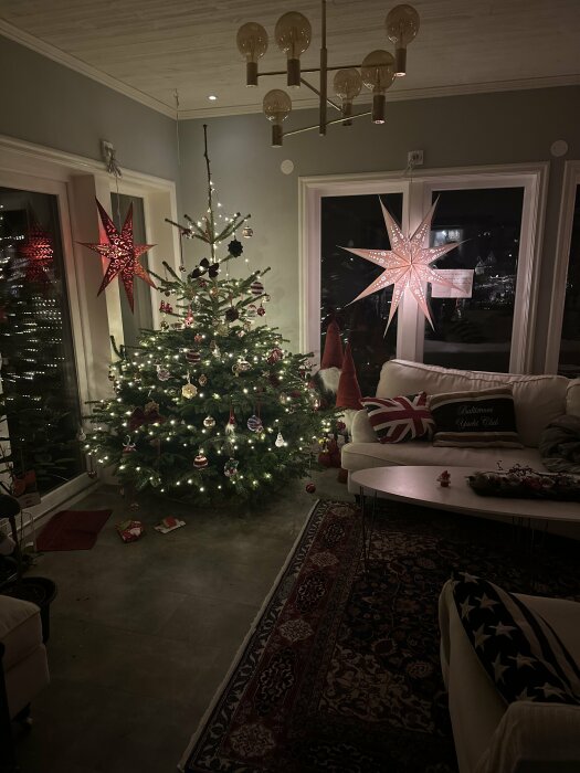 Ett mysigt juldekorerat vardagsrum med julgran, stjärnformade fönsterlampor och förpackade julklappar.